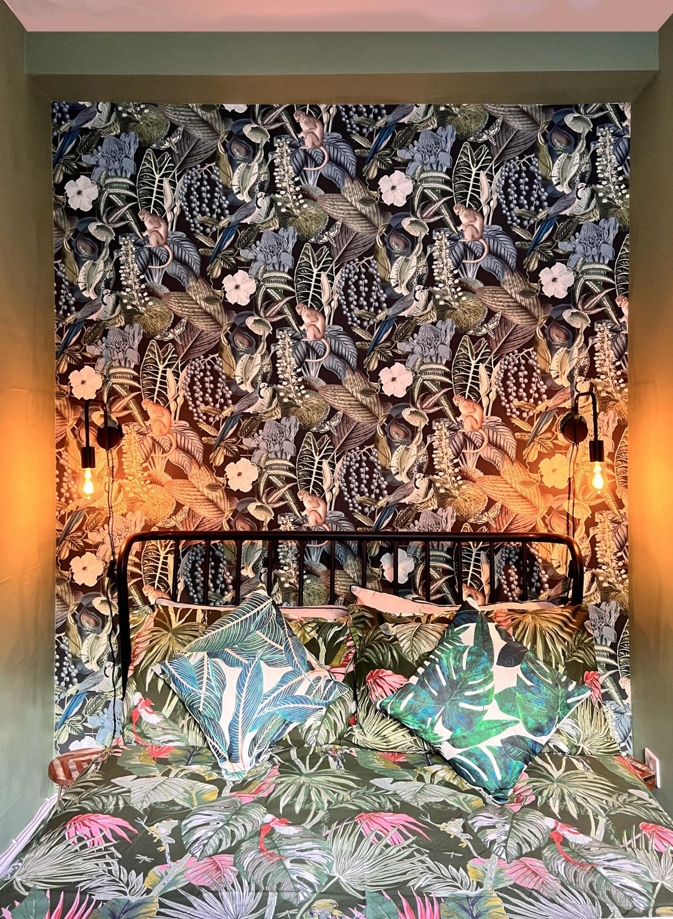 Bed in an alcove of botanical wallpaper, lit by warm lamps